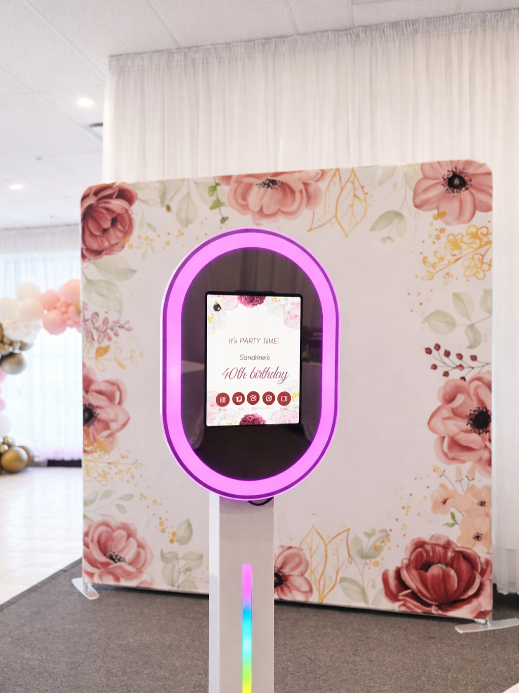 Illuminated mirror photobooth in front of a floral backdrop